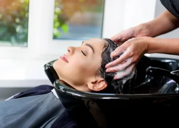 Mujer joven sonriendo en una peluquería chilena mientras le realizan un lavado de cabello relajante antes de un tratamiento hidratante.
