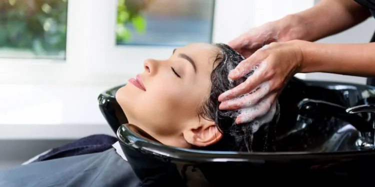 Mujer joven sonriendo en una peluquería chilena mientras le realizan un lavado de cabello relajante antes de un tratamiento hidratante.